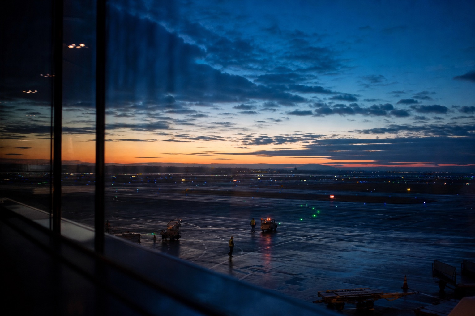 Pre-dawn view of runway lights and ground crew from a terminal window